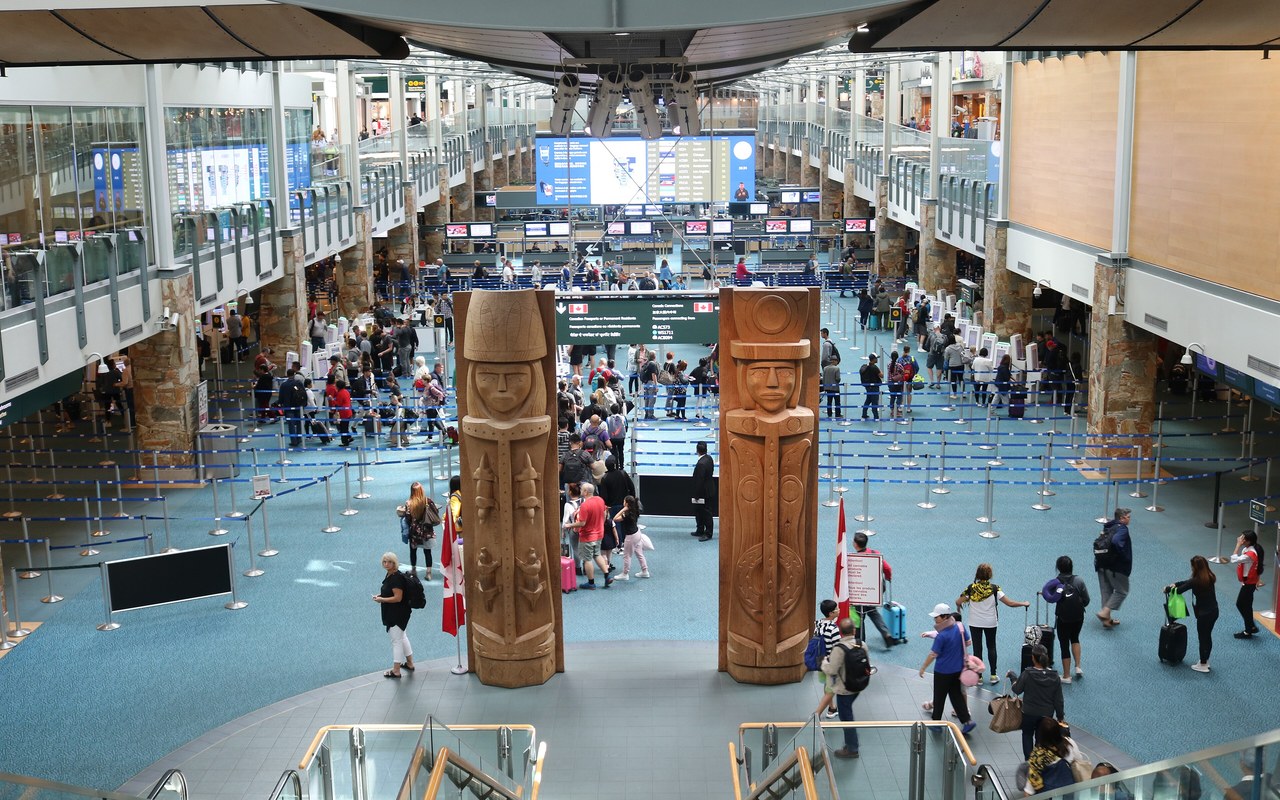 Travellers walking through a busy international airport arrivals hall with luggage